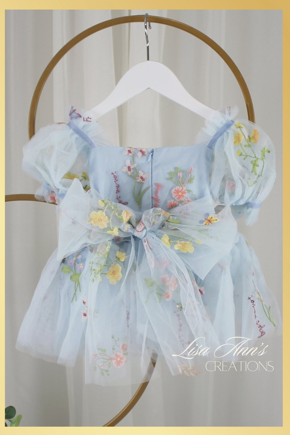 Back of dress showing a tulle floral tied bow. Dress made with built in bodysuit and a light blue floral tulle print on dress. 