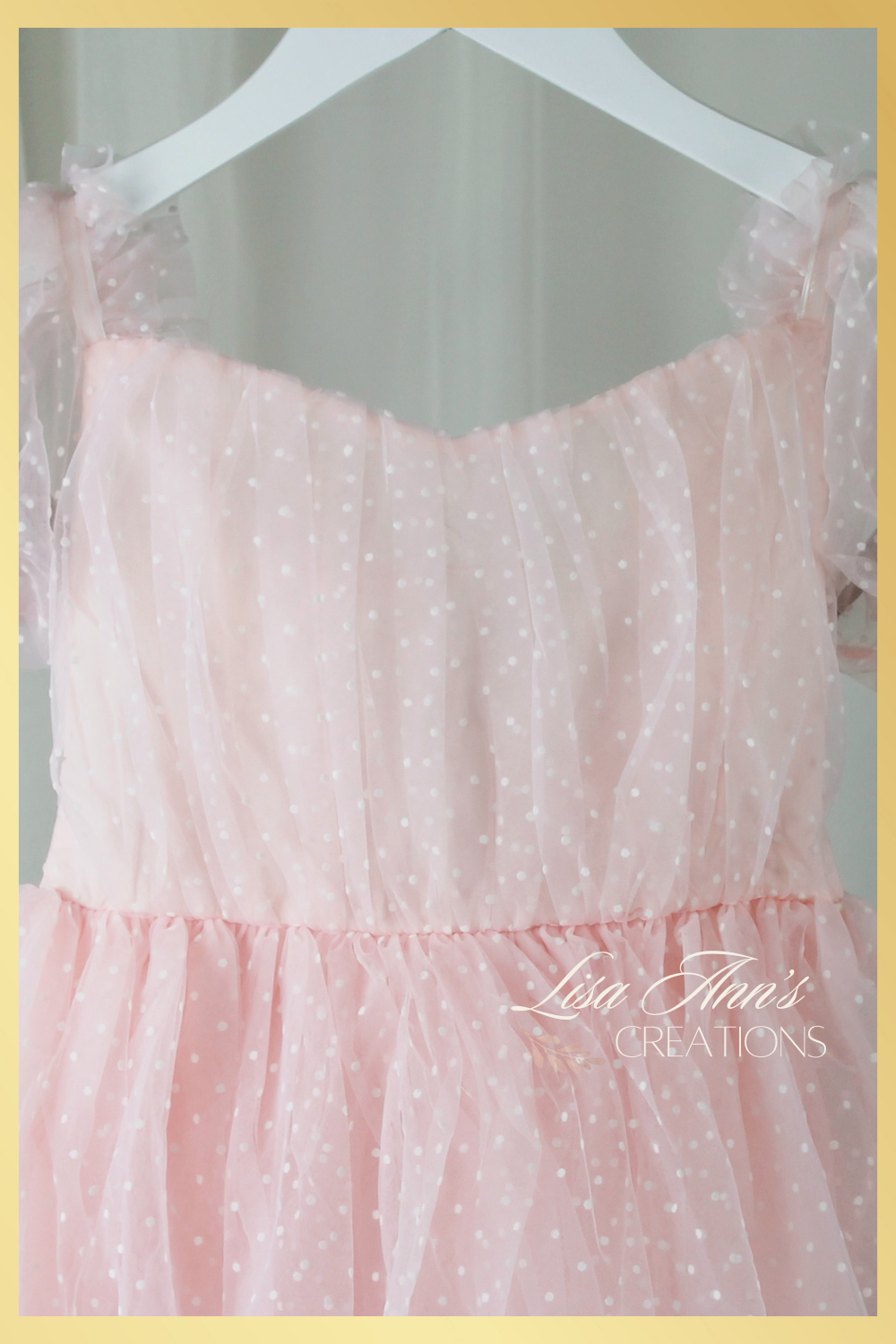 White swiss dot pattern on light pink tulle. Dress has short puffy sleeves and is made to be worn at knee length. 